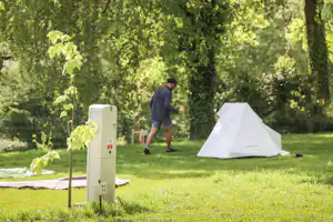 Campingplatz-Parzelle mit Nummer 8, im Hintergrund ein Zelt und ein Mann auf einer grünen Wiese zwischen Bäumen.