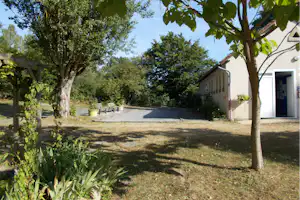 Rasenfläche mit Kiesweg und Bäumen, daneben ein weißes Gebäude mit Türen und Fenstern im Campingbereich.