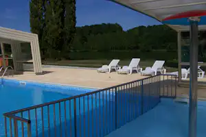 Schwimmbecken auf dem Campingplatz mit Geländer, mehreren Liegestühlen und Blick auf Bäume und Wiesen.