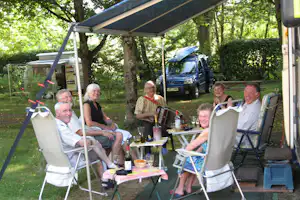 Camping du Lac - Camper sitzen vor dem Wohnmobil im Schatten der Markise