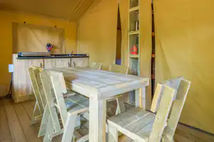 Holztisch mit Bank und Stühlen in einem Campingzelt, daneben Küchenzeile mit Spüle und Wasserhahn.