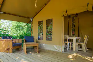 Zelt-Terrasse mit Holzbank, blauen Kissen und Tisch, an der Zeltwand hängen Lampen und Bilder.