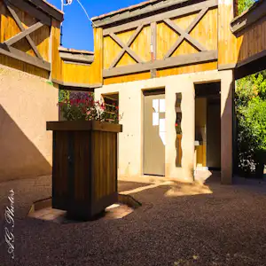 Holzveranda und Eingang eines Campinghauses mit Blumenbeet und Holztür, umgeben von Mauern und Kiesboden.