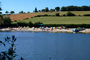 Blick auf einen See mit Liegen und Sonnenschirmen am Ufer, im Hintergrund Wiesen und Bäume.