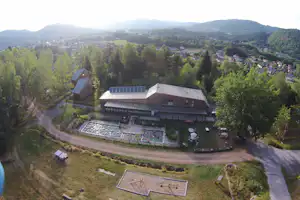 Campinganlage im grünen Tal mit großen Gebäuden, mehreren Stellplätzen, Wegen und umgebenden Bäumen.