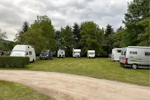 Wohnmobile und Campingbusse stehen auf einem gepflegten Rasenplatz, umgeben von Hecken und Bäumen.