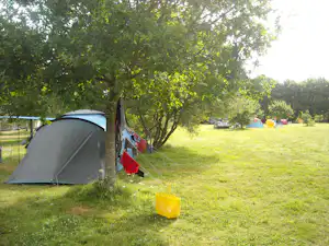 Zelt auf einem grünen Campingplatz, im Hintergrund weitere Zelte und Autos, Bäume spenden Schatten.