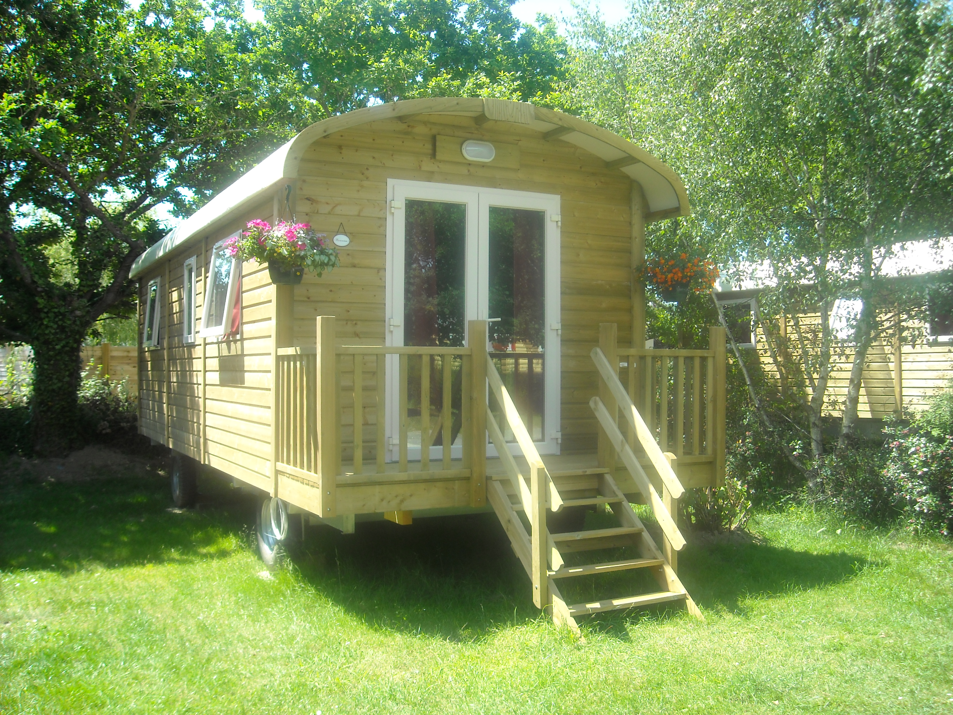 Holzbungalow mit Terrasse und Treppe im Grünen, umgeben von Bäumen und Rasenfläche.