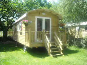Holzbungalow mit Terrasse und Treppe im Grünen, umgeben von Bäumen und Rasenfläche.