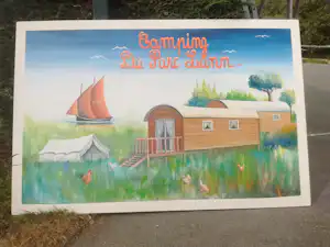 Illustration auf einem Campingplatz-Schild mit Zelt, Wohnwagen und Grasfläche, im Hintergrund Bäume und ein See.