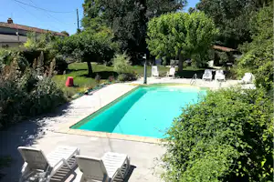 Schwimmbecken auf dem Campingplatz mit weißen Liegestühlen, umgeben von Hecken und Bäumen im Garten.
