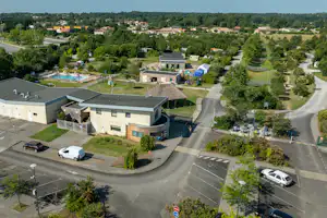 Luftaufnahme einer Campinganlage mit Gebäuden, Stellplätzen, Wegen, Bäumen und mehreren blauen Pools im Hintergrund.