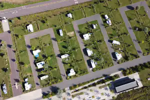 Luftaufnahme von Campingstellplaetzen mit Wohnmobilen und Wohnwagen, dazwischen Wege und Rasenflaechen.