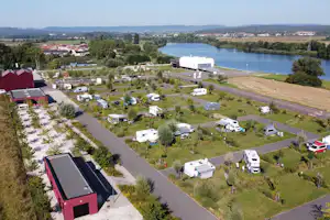 Campingplatz mit Wohnwagen und Stellplätzen am Fluss, große weiße Zeltkuppel und Zufahrtsstraße im Grünen.