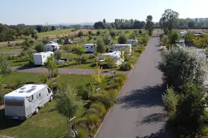 Wohnmobile auf einem Campingplatz, gepflasterte Wege und Stellplätze im Grünen mit Bäumen und Rasenflächen.