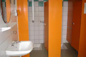 Camping-Badezimmer mit weißem Waschbecken, Spiegel und orangefarbenen Trennwänden, gefliestem Boden und Wänden.