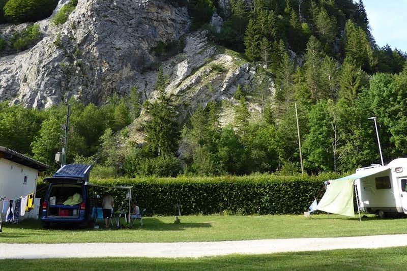 Camping du Val-de-Travers - Wohnwagen und Camping Bulli auf Stellplätzen vor einem Felsen
