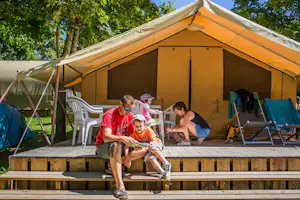 Camping du Ventoulou - Glamping Safarizelt mit Veranda auf der eine Familie sitzt