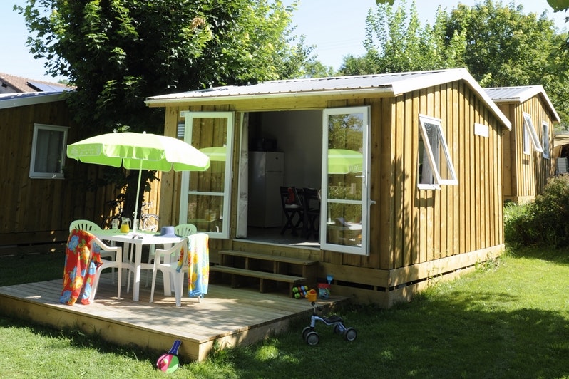 Camping du Ventoulou - Mobilheim mit Veranda, auf der Stühle ein Tisch und ein Sonnenschirm stehen