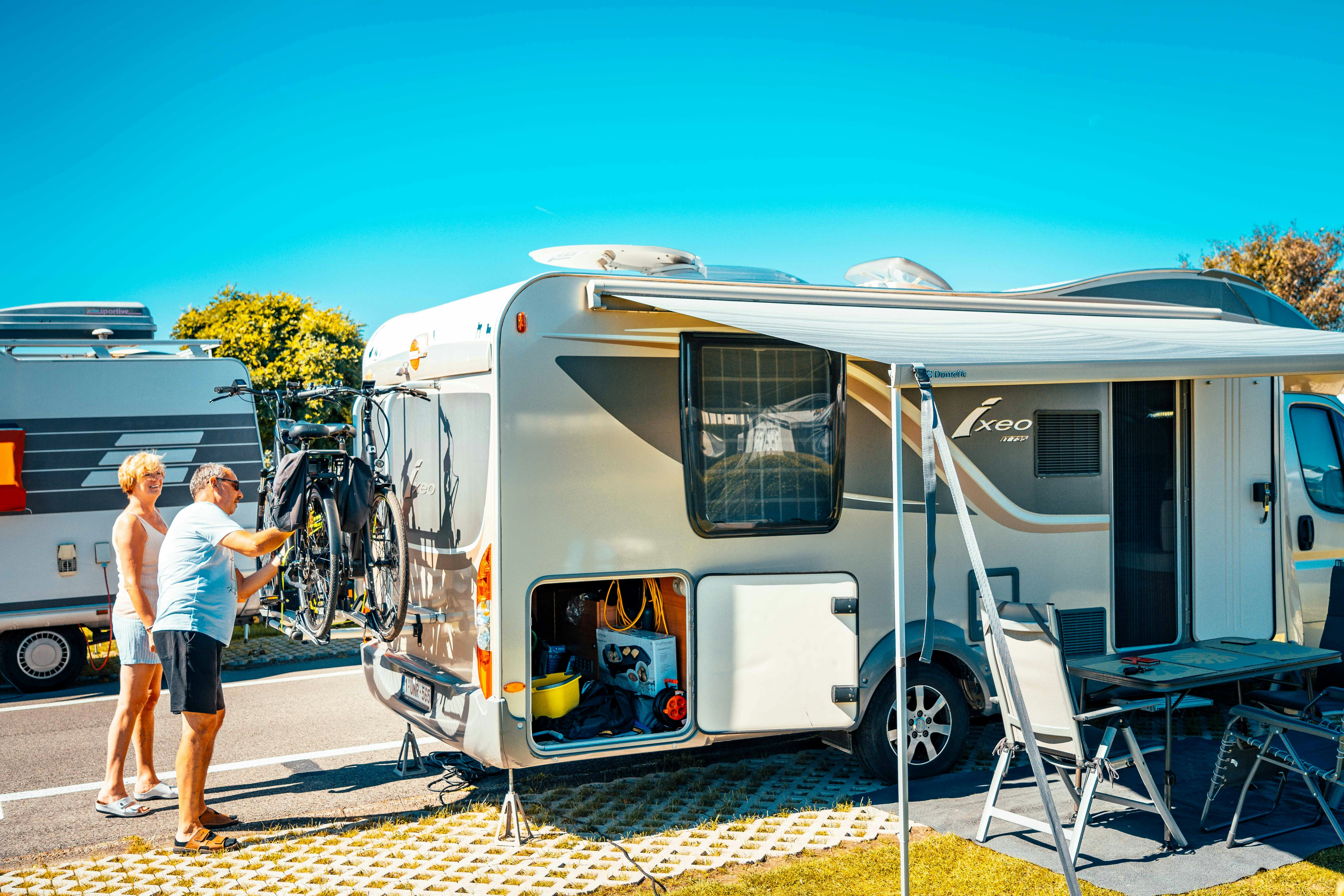 Wohnmobil mit Markise, Fahrrädern am Heck und Leiter am Eingang, daneben ein weiteres Fahrzeug auf dem Campingplatz.