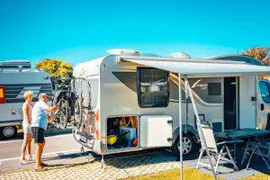 Wohnmobil mit Markise, Fahrrädern am Heck und Leiter am Eingang, daneben ein weiteres Fahrzeug auf dem Campingplatz.