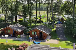 Zwei Holz-Campinghütten mit Schiebedach, gepflegtem Rasen und Wegen im grünen Campingplatz, daneben geparkte Autos.