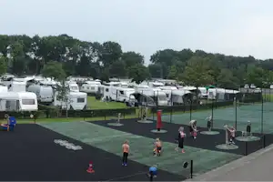 Campingplatz mit Wohnmobilen und Stellplätzen, gepflegtem Rasen, Spielbereich und Blick auf Bäume im Hintergrund.