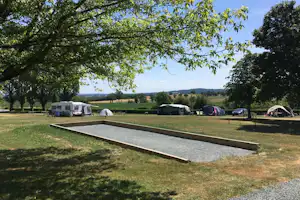 Stellplätze auf einem Campingplatz mit Wohnwagen und Zelten, Rasenfläche, Hecken und Bäumen am Rand.
