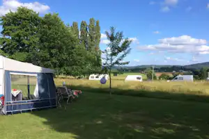 Zelt auf einem grünen Campingplatz mit Sitzbank und Bäumen, im Hintergrund weitere Wohnwagen und Wiesen.