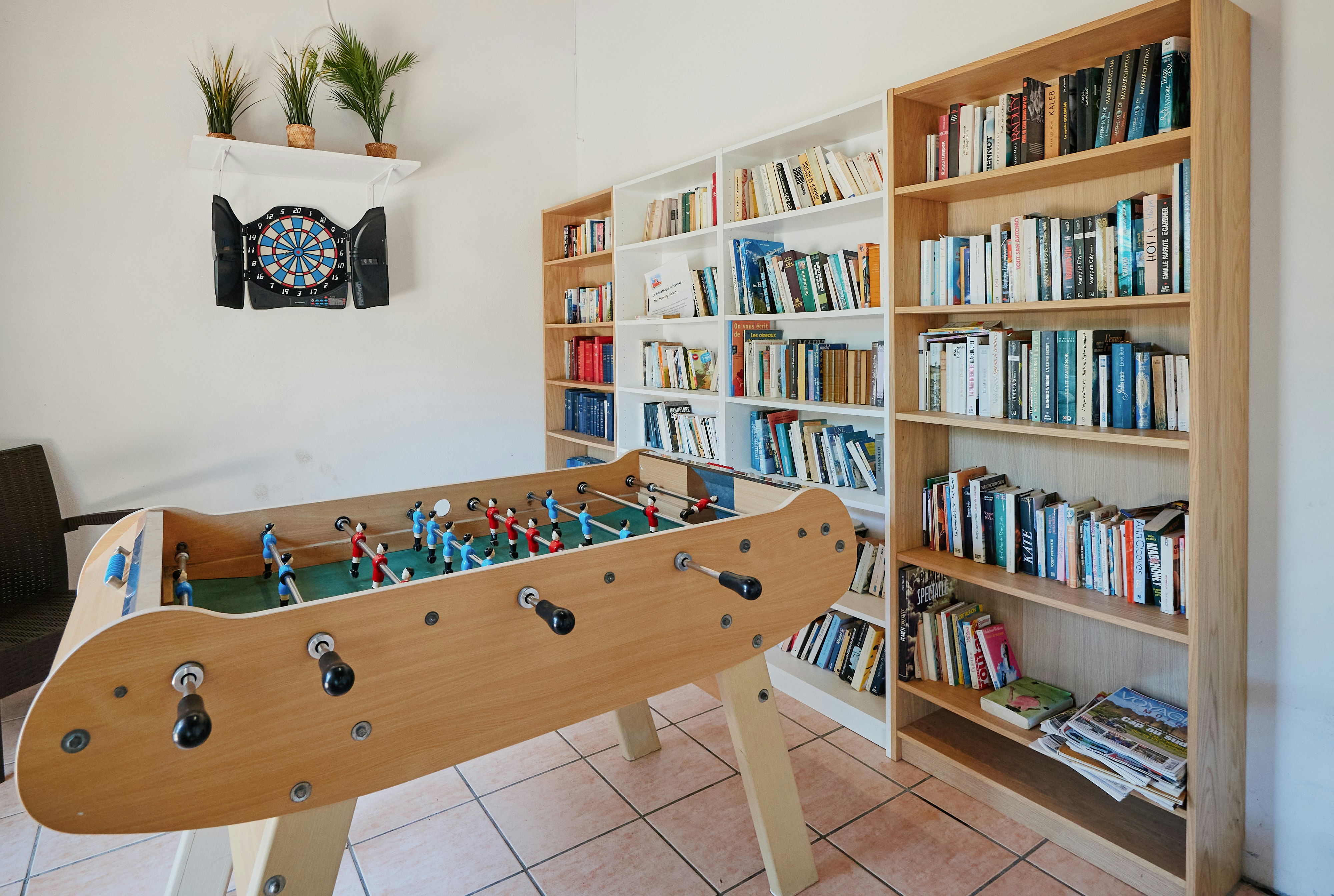 Billardtisch im Innenraum mit Holzdecke, Bücherregal und Wanddeko, auf gefliester Terrasse im Campinghaus.