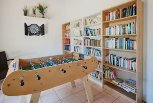 Billardtisch im Innenraum mit Holzdecke, Bücherregal und Wanddeko, auf gefliester Terrasse im Campinghaus.