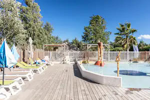 Pool auf einer Holzterrasse mit Sonnenliegen und Sonnenschirmen, umgeben von Zäunen und Bäumen.