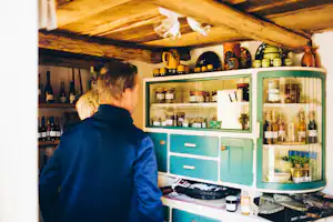 Campingküche mit offenen Regalen, Geschirr und Gewürzen, Holzdecke und eine Person vor der Küchenzeile.