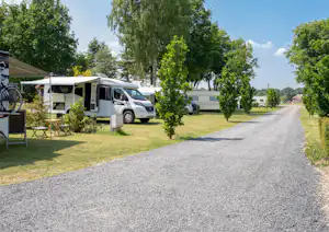 Wohnmobil auf dem Stellplatz, daneben Tisch und Stühle, Bäume entlang des Kieswegs im Campingbereich.