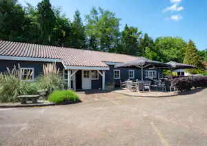 Ferienhaus mit Terrasse, Sitzgruppe und Markise vor dem Eingang, umgeben von Büschen und Bäumen.