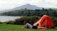 Camping Eagle Point - CAmper liegt vor seinem Zelt am Wasser und liest