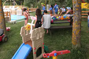 Kinder spielen auf dem Campingplatz: Spielgeräte, bunte Bälle und ein kleiner Pool im Garten mit Holzzaun.