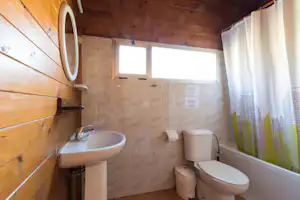 Modernes Badezimmer in einem Holzhaus mit Waschbecken, Toilette, Dusche und Vorhang, hellen Fliesen und Wandpaneelen.