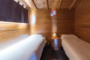 Holzunterkunft mit zwei Betten, Nachttischen und Lampen, Blick in den Innenraum mit Deckenbalken.