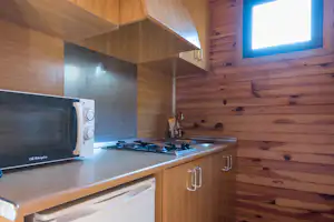 Holzwohnwagen mit Küchenzeile: Spüle, Herd und Kühlschrank, darüber Schränke und ein Fenster im Innenraum.