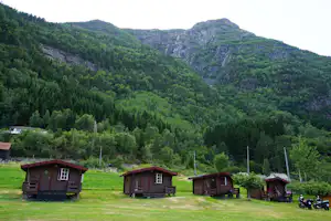 Camping-Häuschen auf einer Wiese im grünen Tal, umgeben von Bäumen und Bergen im Hintergrund.