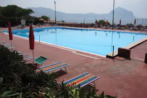 Camping-Pool mit blauen Liegen, Sonnenschirmen und Blick auf Berge im Hintergrund.
