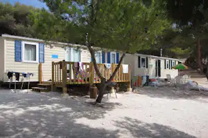Reihe von Mobilheimen am Campingplatz mit Holzterrasse, Markisen und Wäscheleine zwischen Bäumen.