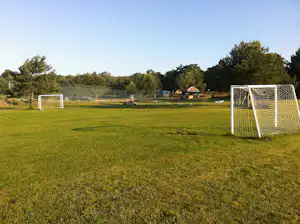 Fußballtor auf grünem Rasen am Campingplatz, im Hintergrund weitere Tore, Bäume und ein kleiner Pavillon.