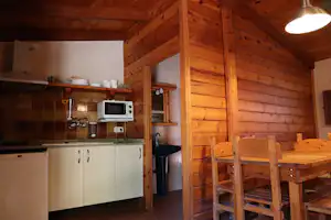 Holzblockhütte mit Küchenzeile und Mikrowelle, Essplatz mit Tisch und Stühlen im Innenraum.