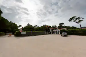 Eingang vom Campingplatz Rosál mit Rezeption, Schranke, Schildern, Parkplatz und Bäumen unter bewölktem Himmel.