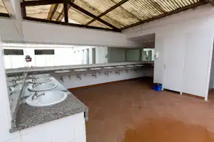 Gemeinschaftsbad mit mehreren Waschbecken, Spiegeln und Fliesenboden, Holzdecke mit Balken und Handtuchhaken an der Wand.
