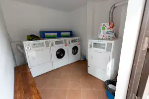 Waschraum mit mehreren Waschmaschinen und Wäschetrocknern, Flachbild-Programmanzeigen und Wäschekorb auf dem Boden.