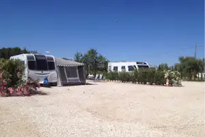 Wohnwagen auf einem Campingplatz mit Kiesfläche, Hecken und mehreren Stellplätzen im Hintergrund.