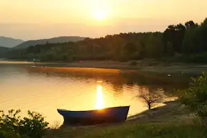 Boot am Ufer eines Sees beim Sonnenuntergang, umgeben von Bäumen und Hügeln in der Ferne.
